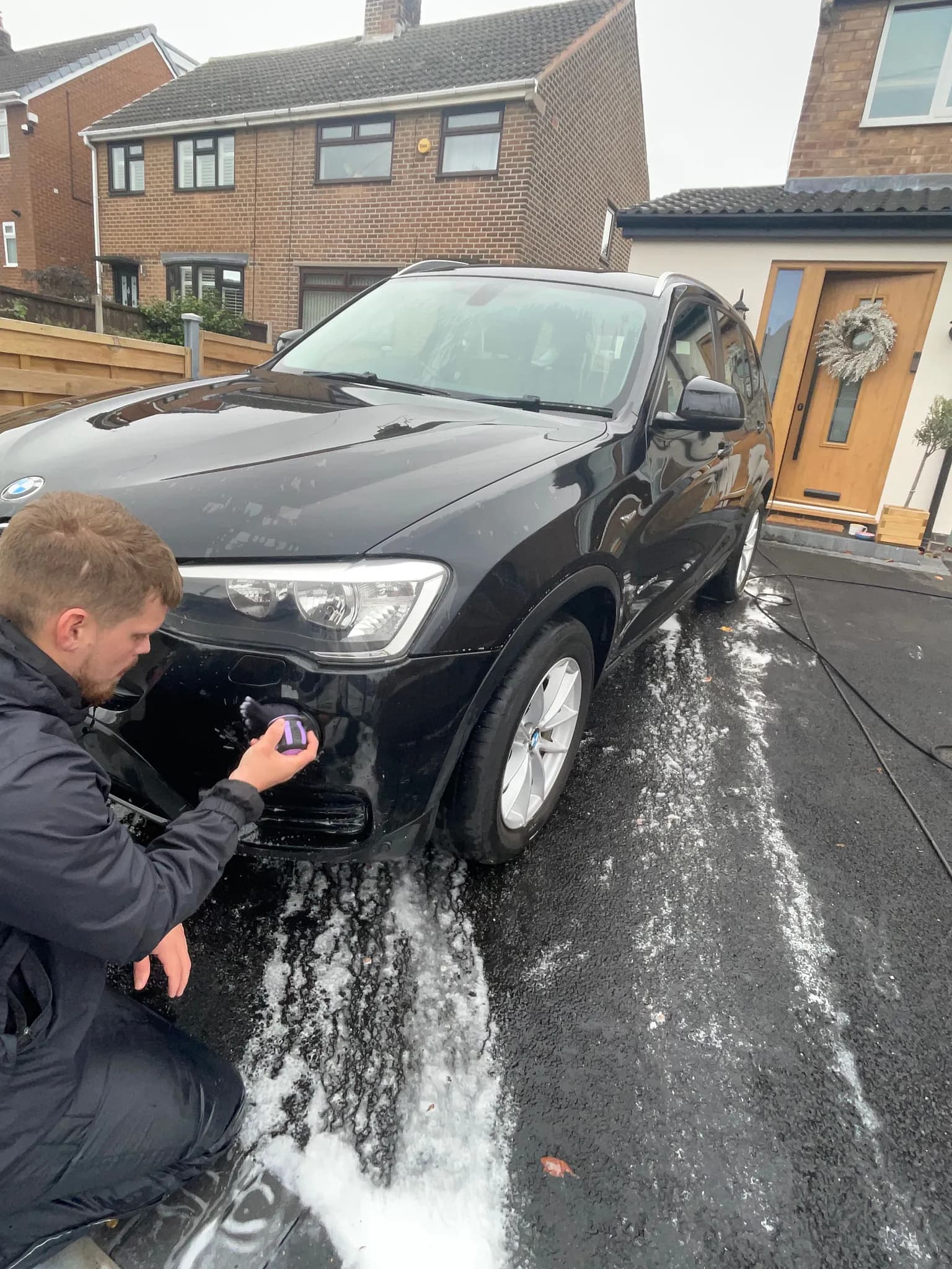 Cameron Duffy of DRC Car Care cleaning the front bumper of a black BMW with a detailing brush