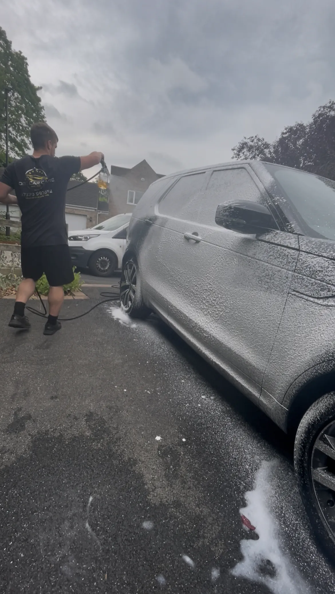 Cameron Duffy of DRC Car Care covering a grey SUV in snow foam on a driveway