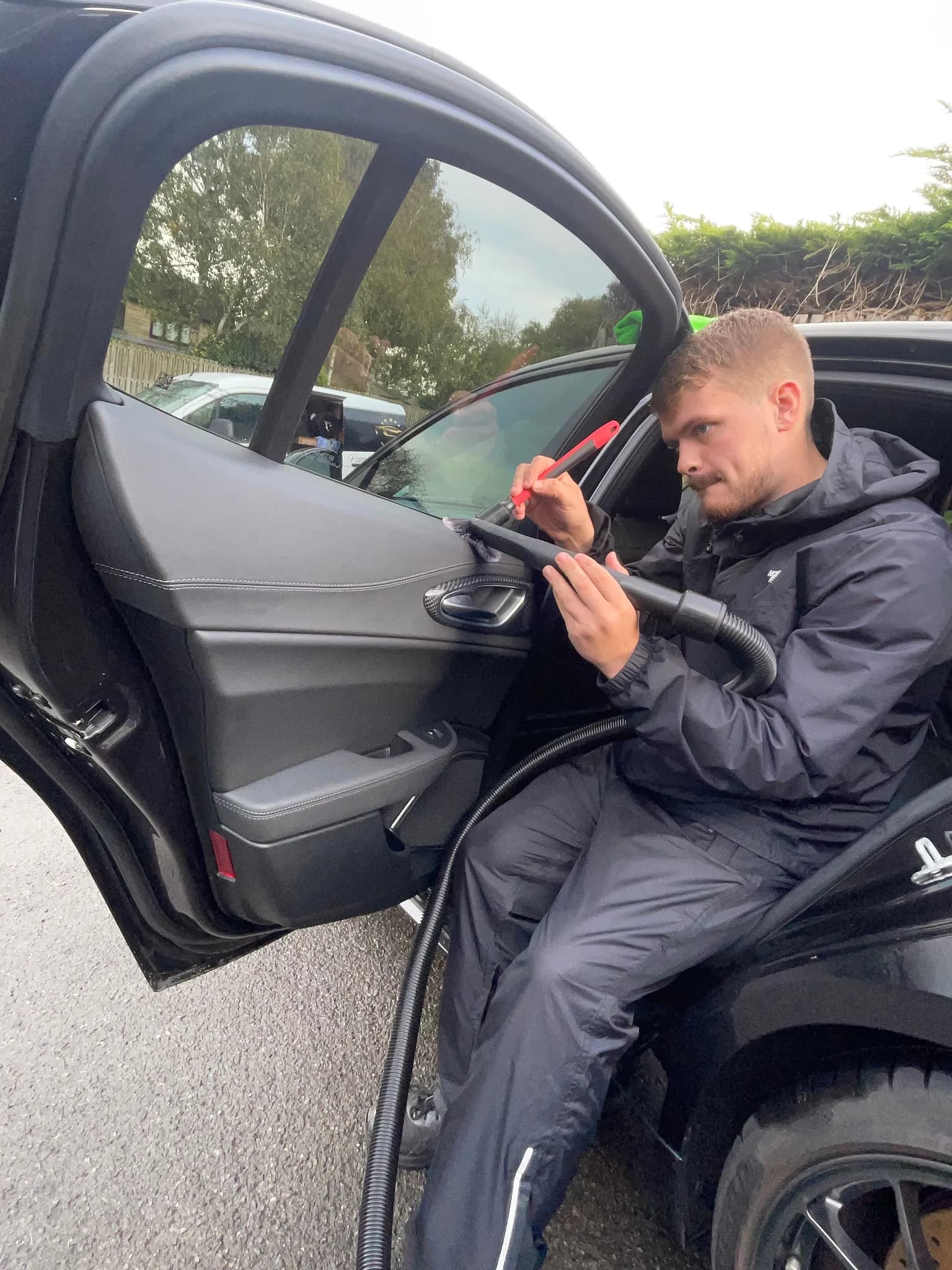 Cameron Duffy of DRC Car Care vacuuming and brushing the door card of a black car